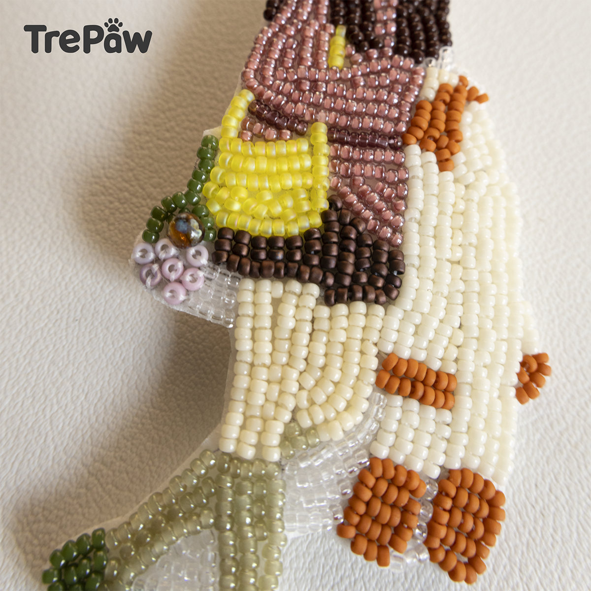 Close-up of Miss Antelope bead embroidery showing the rose-colored turtleneck, orange hat, and tiny bouquet on her yellow bag.