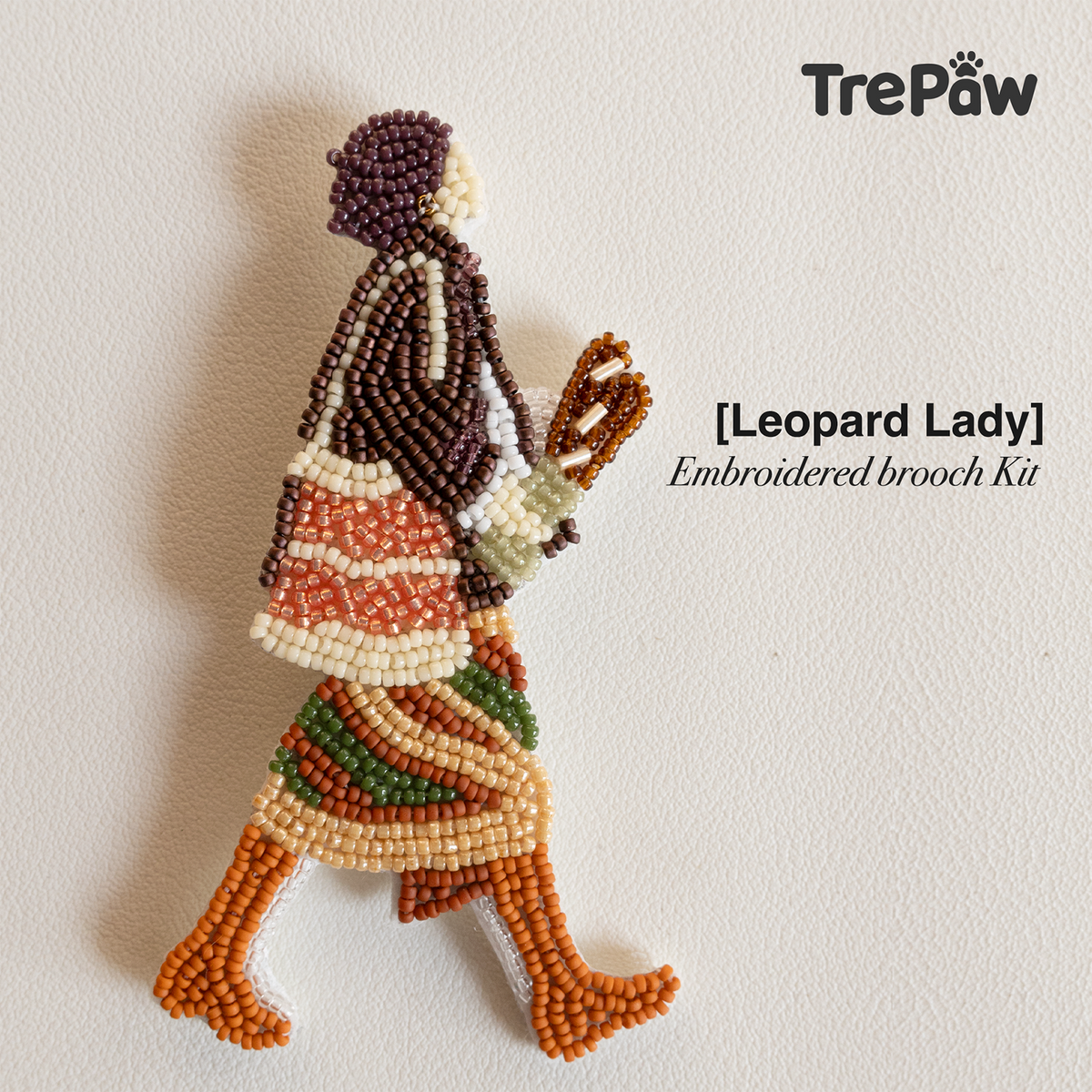 Leopard Lady handmade bead embroidery brooch featuring a short-haired woman in a burgundy top and leopard-print skirt holding a baguette.