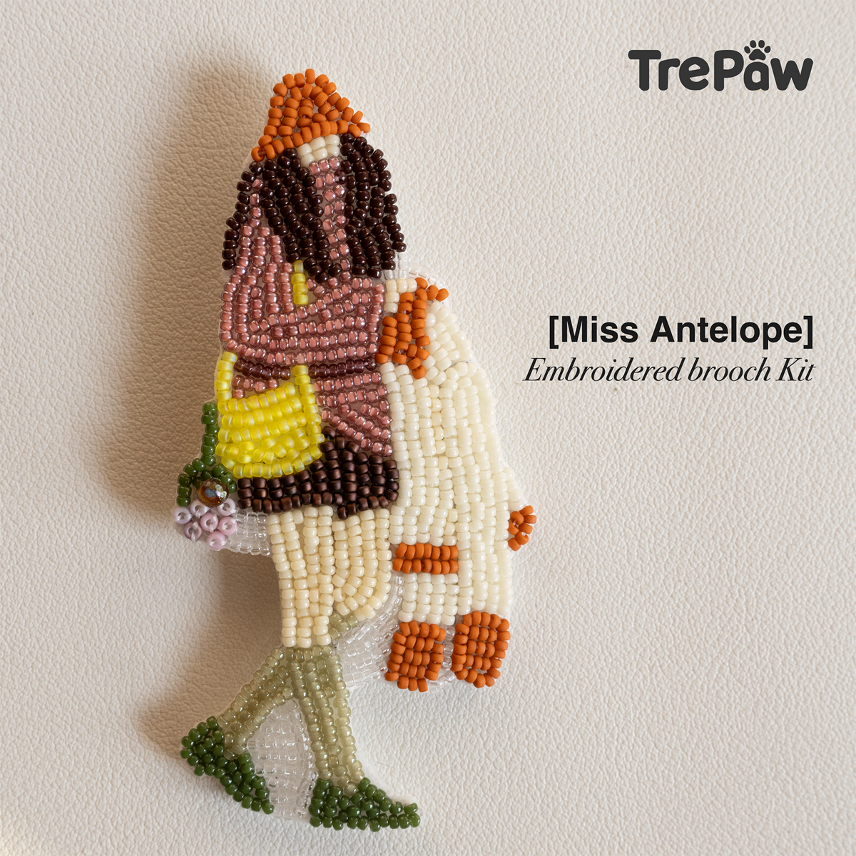 Miss Antelope handmade bead embroidery brooch featuring a curly-haired woman in a rose turtleneck and orange hat carrying a pale yellow bag.